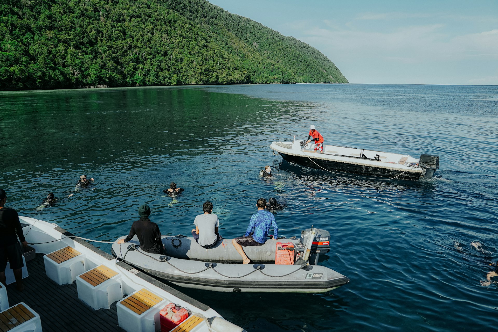 People are swimming in the ocean near boats.